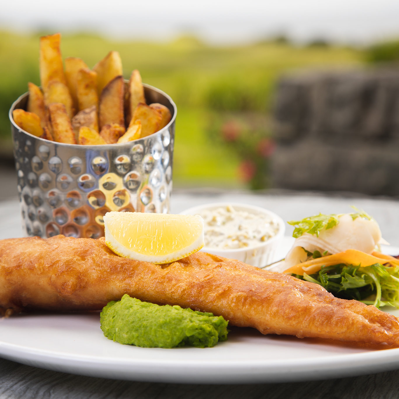 battered fish with lemon wedge, side salad and chips